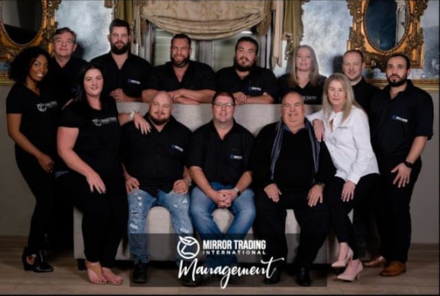 Group photo showing 13 individuals with the text "Mirror Trading International Management" superimposed